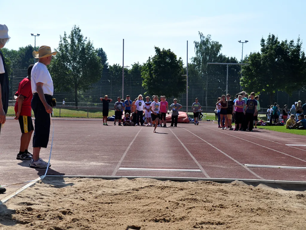 Person mit Sonnenhut steht an der Weitsprunggrube.